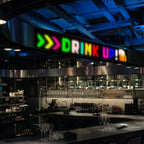 Soft LED sign showing "DRINK UP" above a restaurant bar